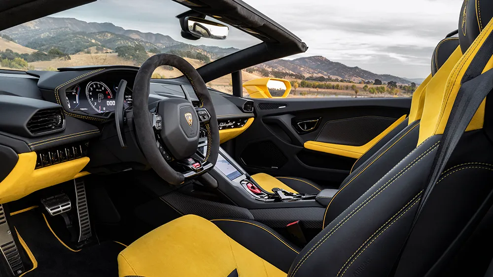 Open-top luxury sports car interior with black and yellow seats, steering wheel, and center console.