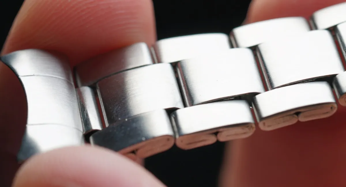 Close-up of stainless steel watch band links being held between fingers, showing the joints and brushed metal surface.