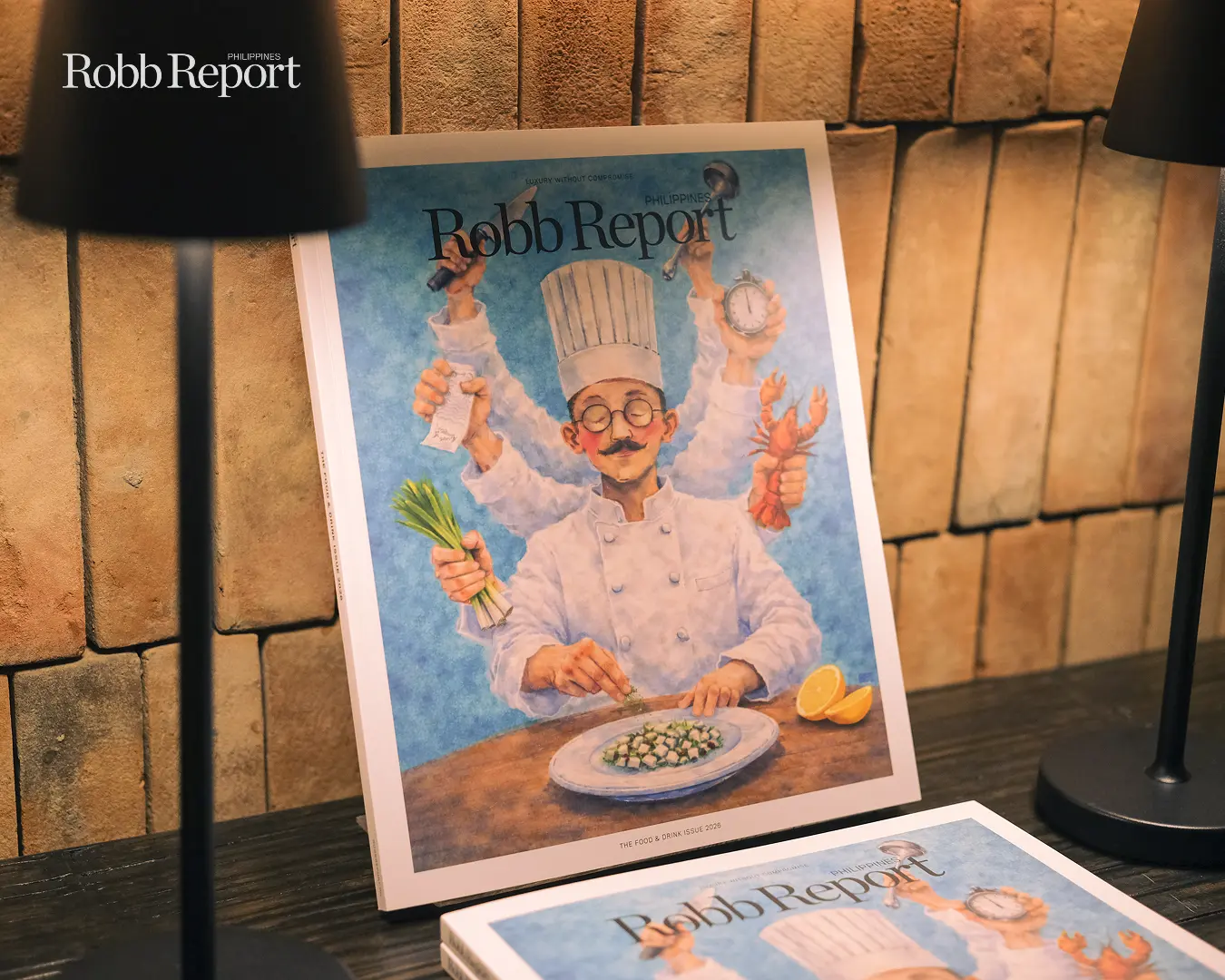 Color illustration of a chef with multiple arms holding kitchen items (leeks, lobster, clock) on a blue background, with 'Robb Report' title at top.