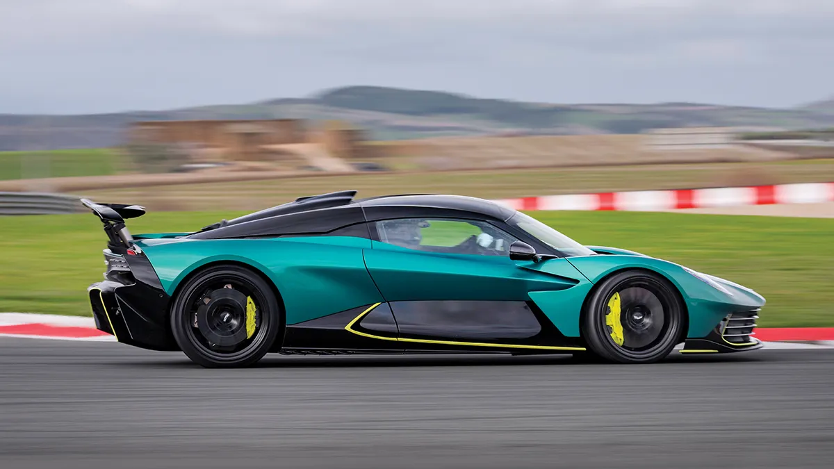 Teal and black high-performance sports car speeding along a race track with yellow brake calipers visible