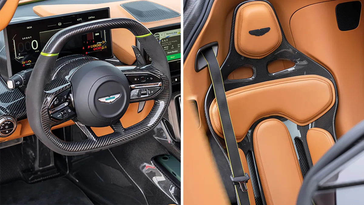 Luxury sports car interior with carbon fiber steering wheel and orange leather trim, Aston Martin emblem visible on the center cap.
