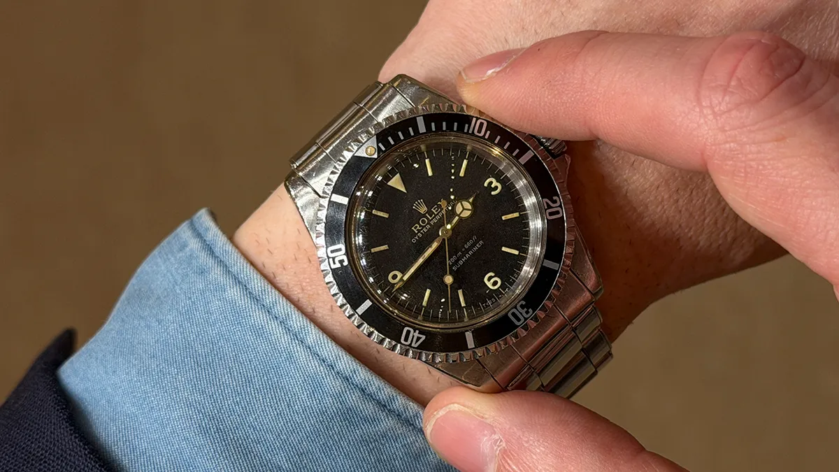 Vintage Rolex Submariner wristwatch on a man's left wrist with a black dial and rotating bezel, metal bracelet.