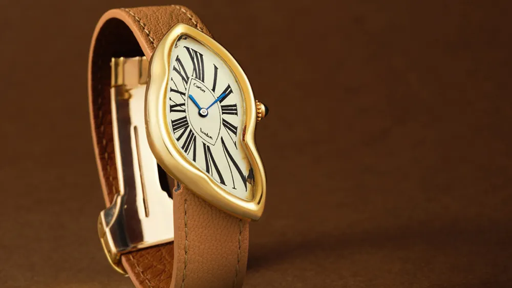 Gold-toned wristwatch with a curved, distorted round dial and a brown leather strap against a brown backdrop.