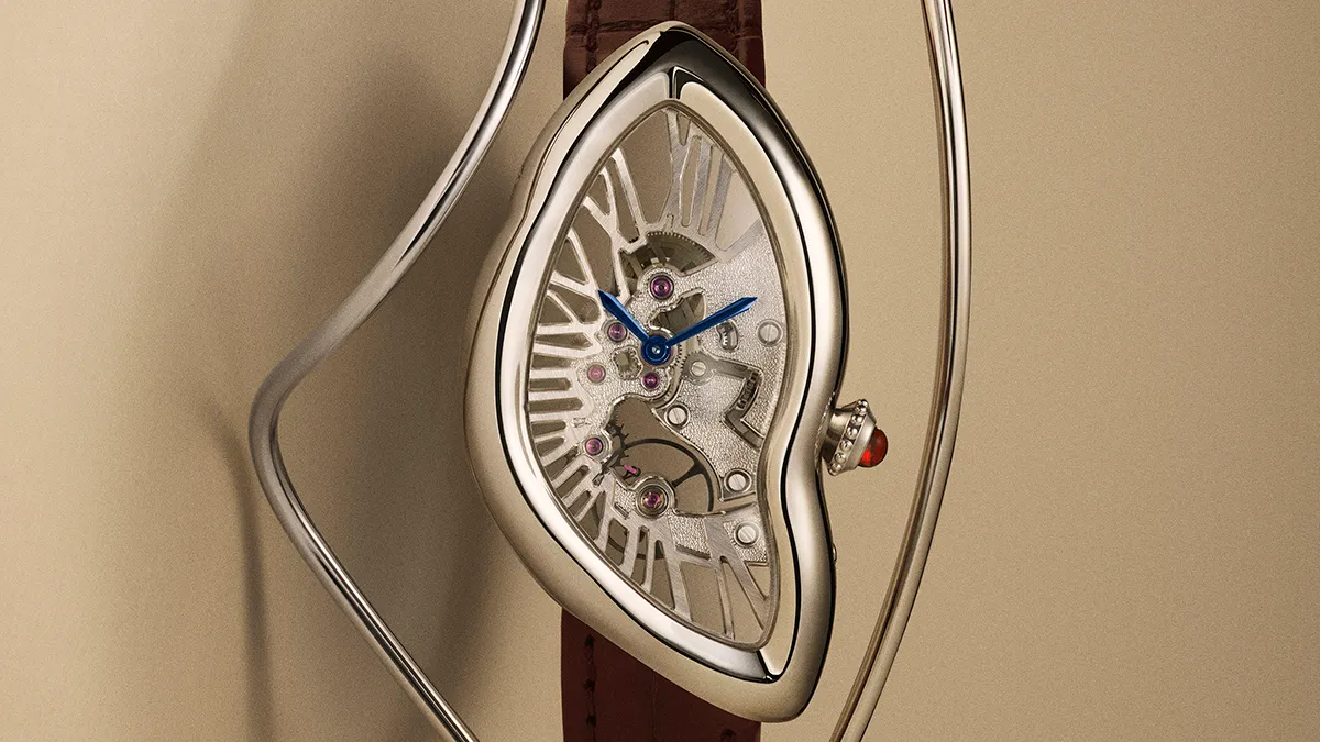 Heart-shaped skeleton wristwatch with blue hands and visible gears, on a brown leather strap against a beige background.