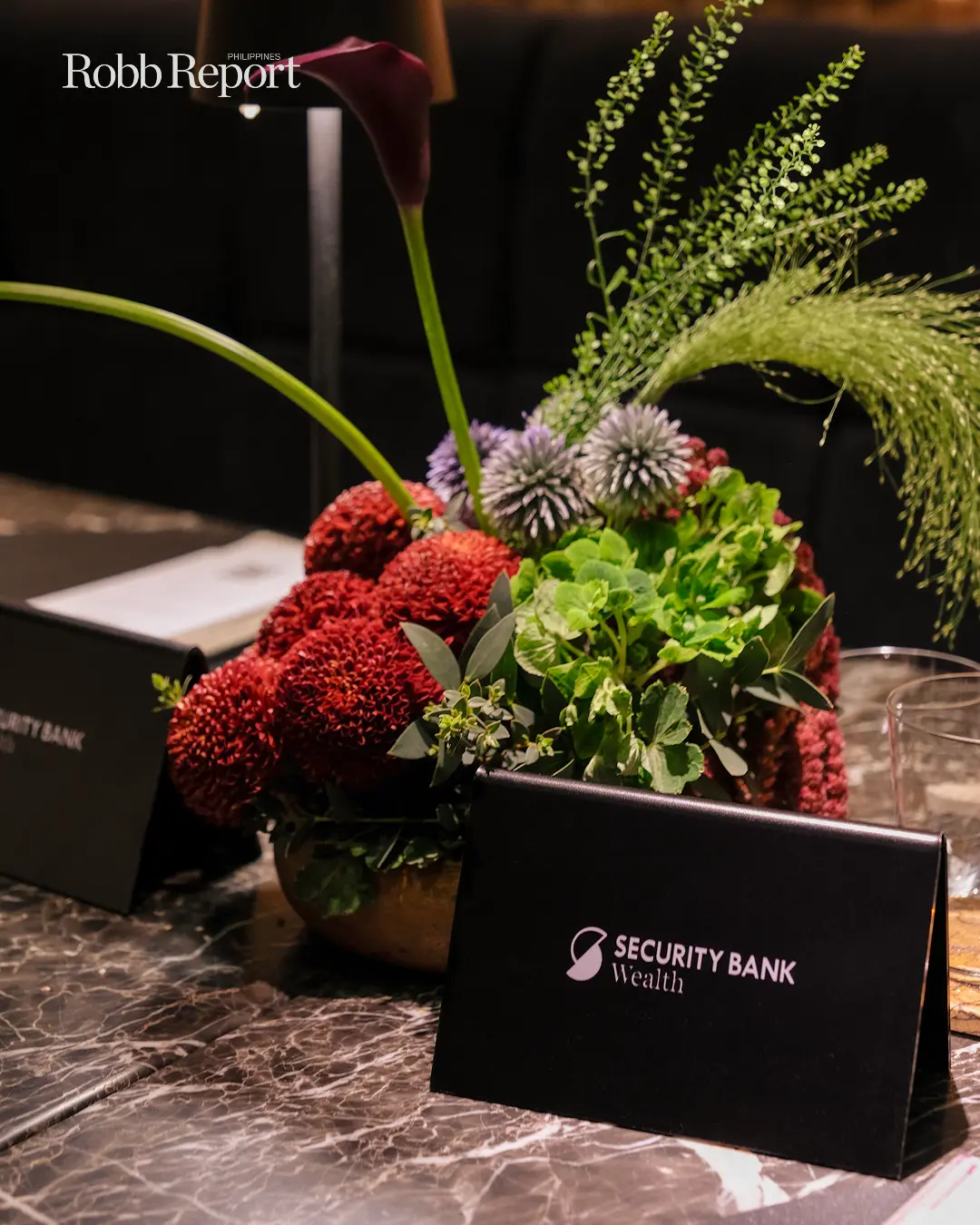 Floral centerpiece with red pom-pom blooms and greenery on a marble table, with a Security Bank Wealth card in the foreground.
