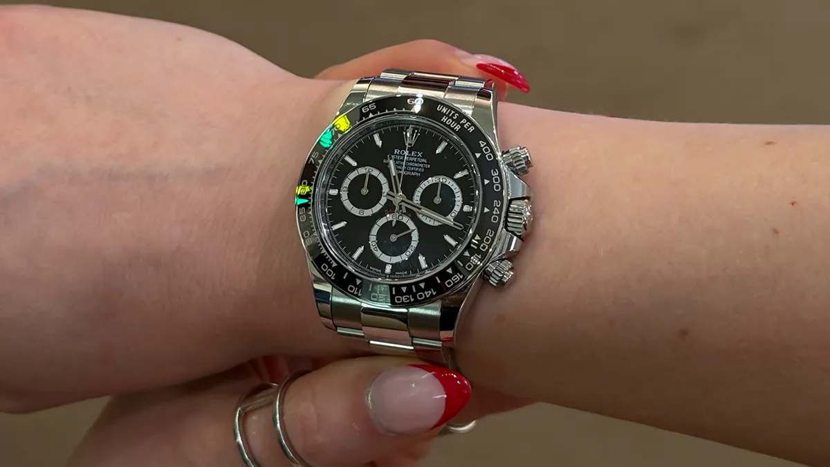Rolex Daytona chronograph on a wrist with a black dial and stainless steel bracelet, showing three subdials and a tachymeter bezel.