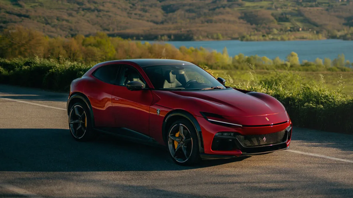Red luxury sports car parked on a scenic road with a lake and green hills in the background.