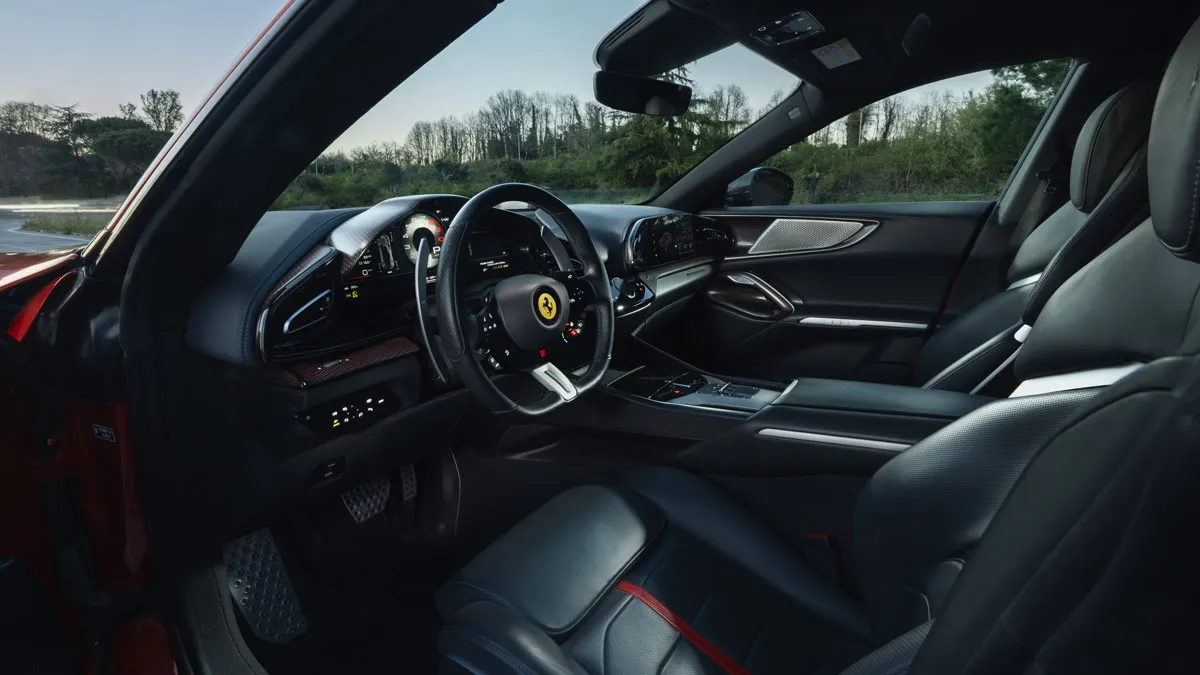 Luxurious black leather interior of a sports car with a multifunction steering wheel, digital instrument cluster, and center console controls, seen from the passenger side.