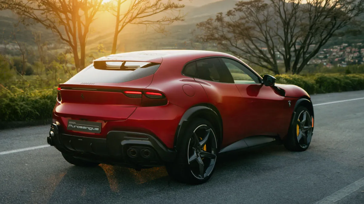 Red Ferrari Purosangue parked on a winding road at sunset, with hills and trees in the background.