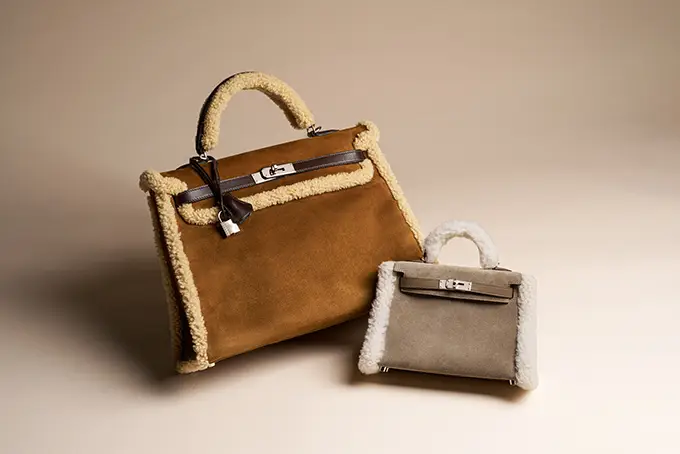 Two suede handbags with fluffy off-white shearling trim, a large brown tote and a smaller gray clutch on a neutral backdrop.