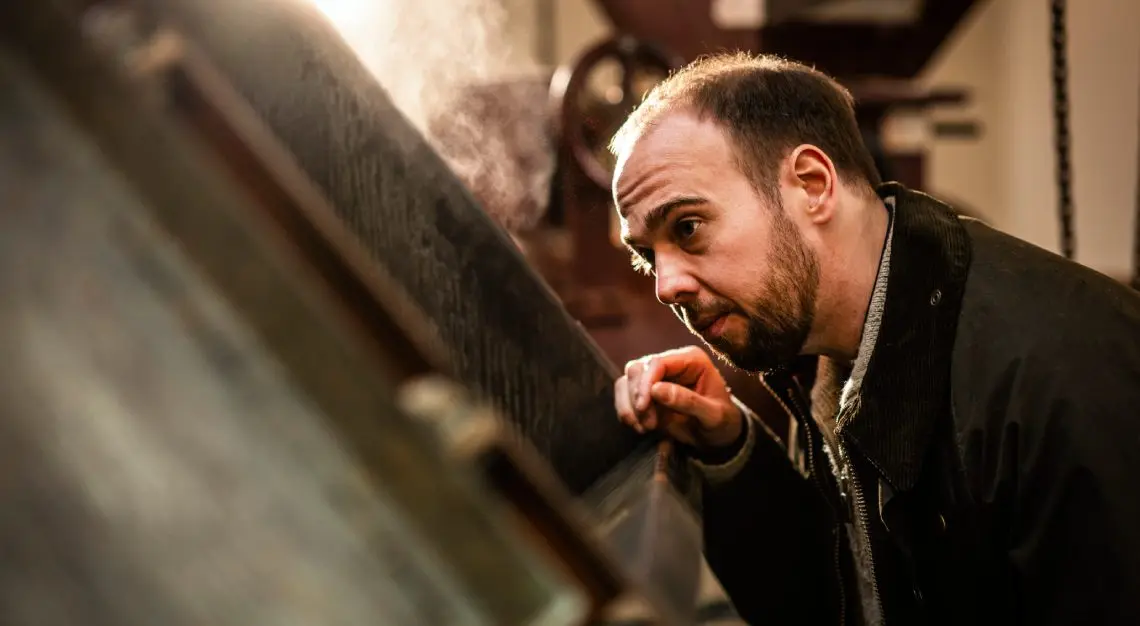 Man with a beard leaning in, closely inspecting a large piece of industrial machinery in a workshop