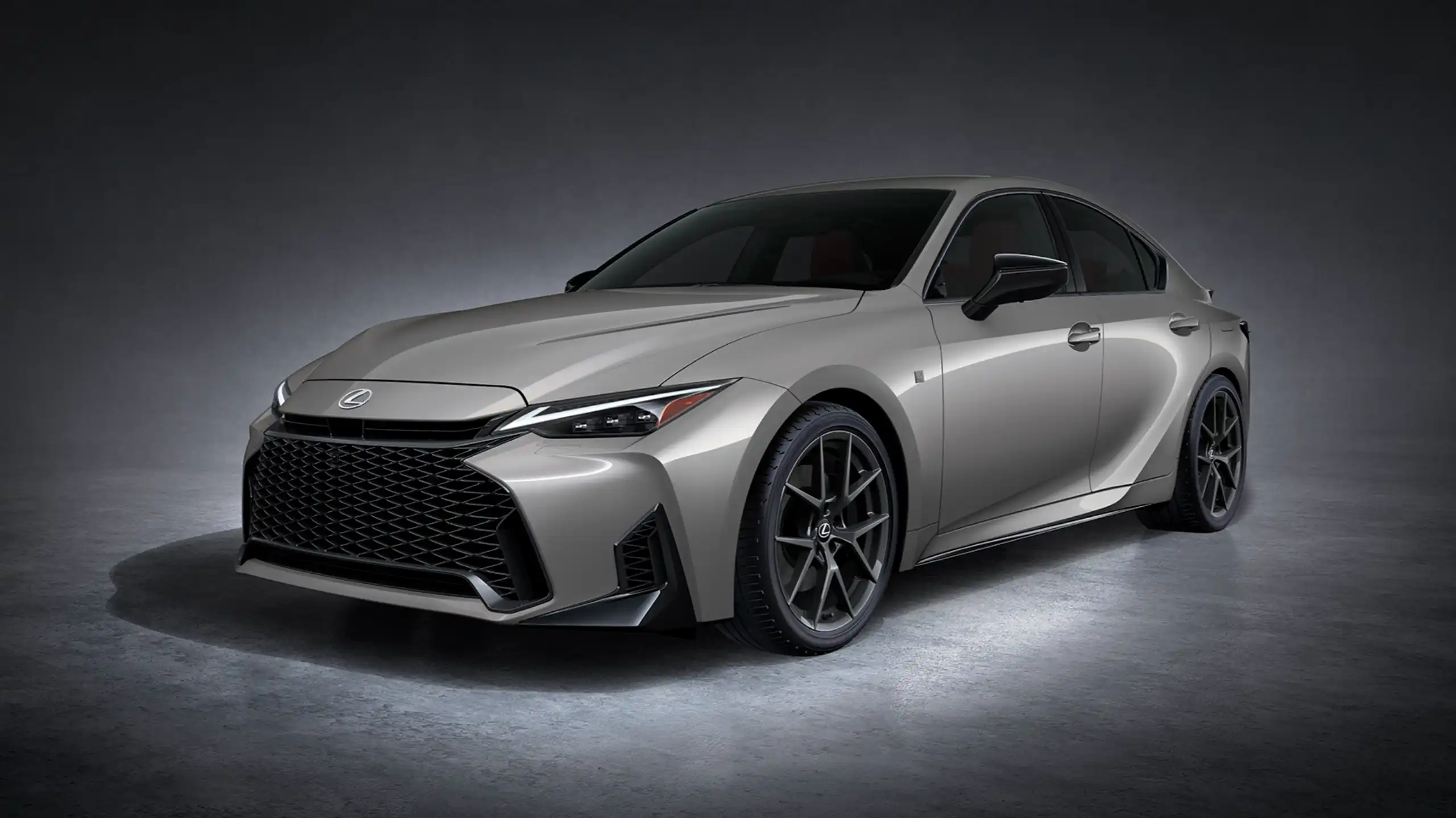 Front three-quarter view of a silver luxury Lexus sedan with a bold black grille and sharp headlights against a dark studio background.
