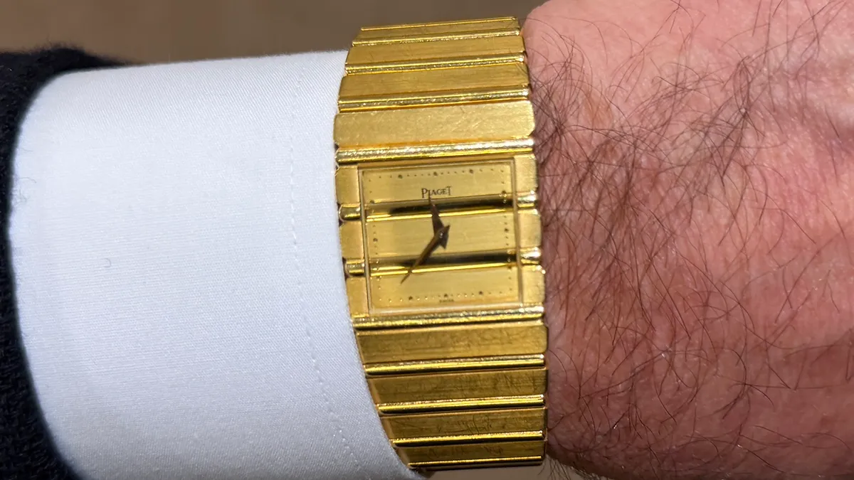 Gold Piaget wristwatch with a segmented bracelet on a man’s wrist, white dress shirt cuff visible at left.