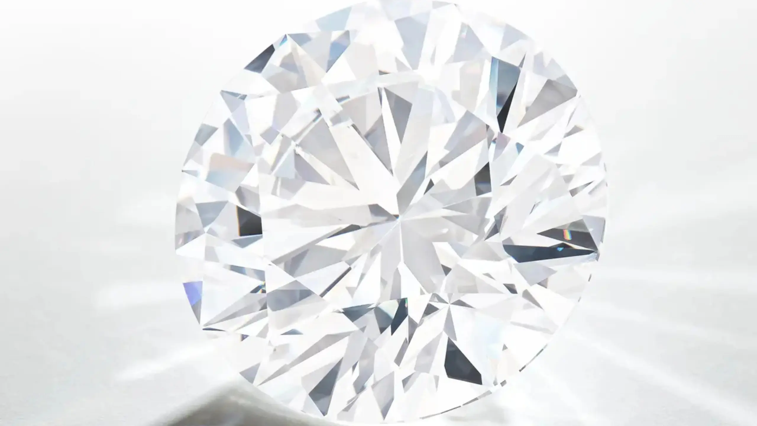 Close-up of a faceted diamond sphere resting on a pale reflective surface, catching light from multiple angles.