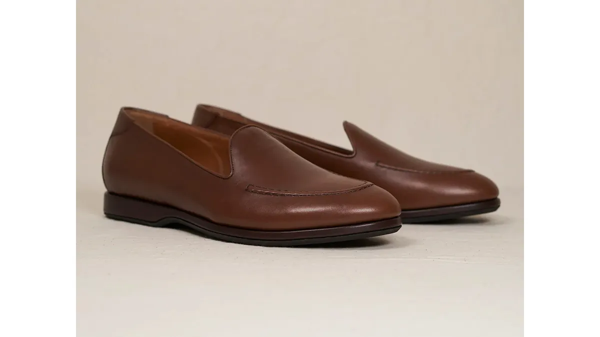Pair of brown leather loafers photographed on a light surface, viewed from the side and slightly front-facing.
