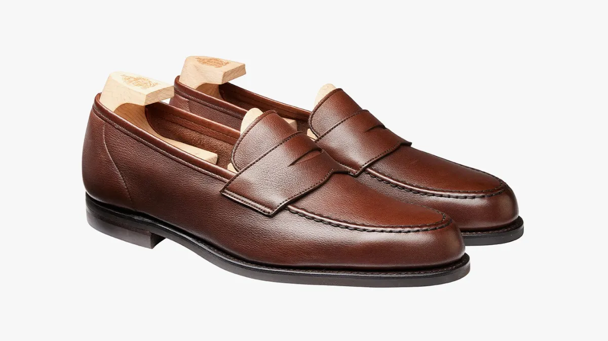 Brown leather penny loafers on a white background with wooden shoe trees inside.
