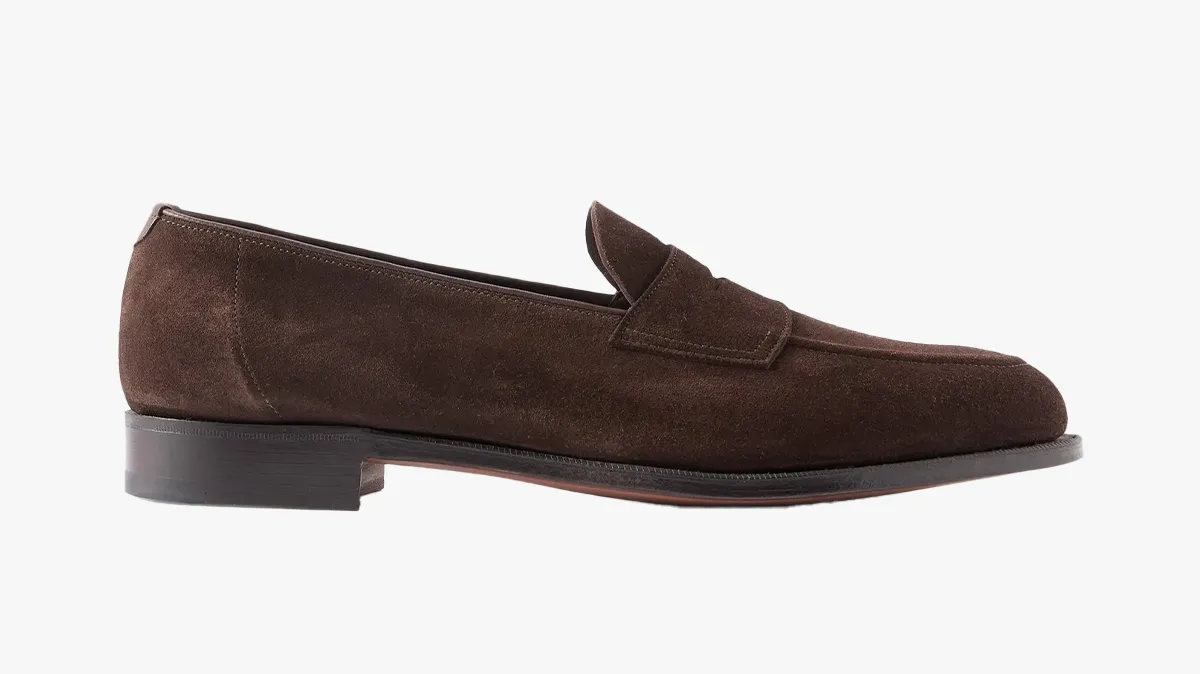 Brown suede penny loafer with a strap across the vamp and a low stacked heel on a white background.