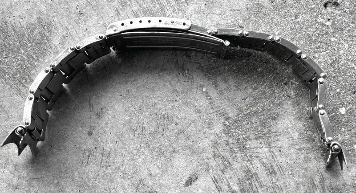 Curved metal watch band laid in an arc on a rough concrete surface.