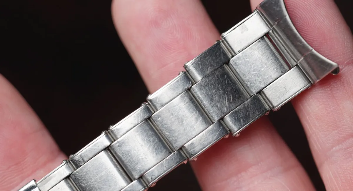 Close-up of a worn stainless steel watch band being held between fingers, showing scratched links.