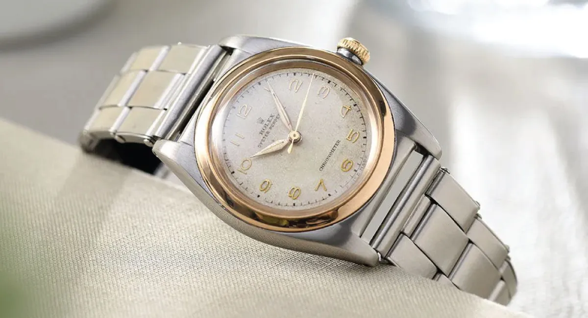 Two-tone metal wristwatch with a gold bezel and silver bracelet resting on light fabric surface.