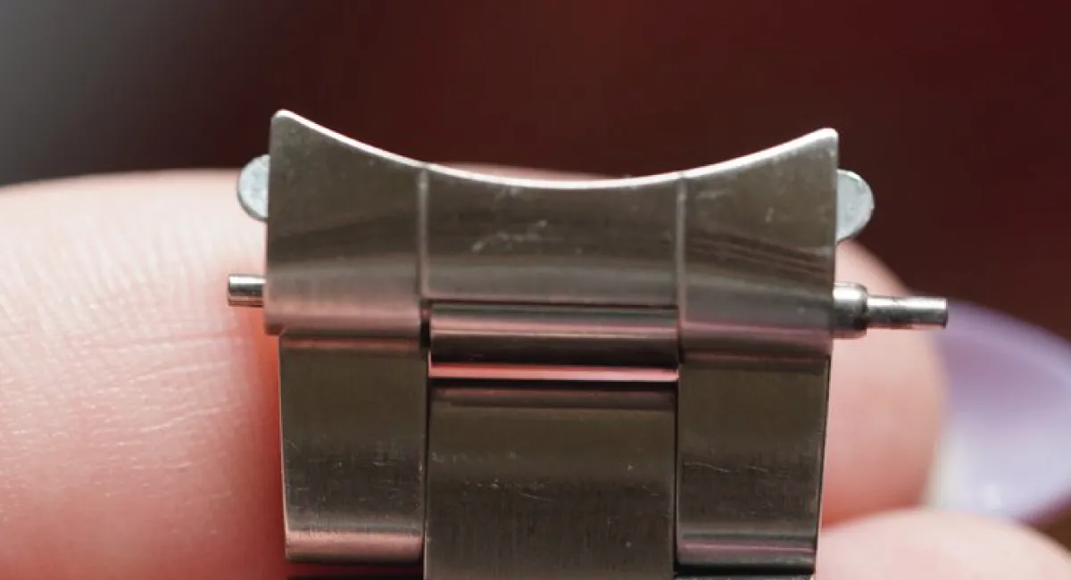 Close-up of a metal watch band clasp with a protruding pin held between fingers