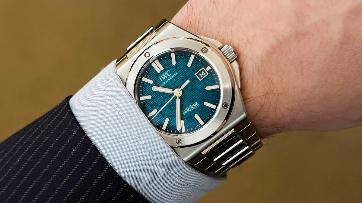Wristwatch with teal dial and stainless steel bracelet on a dress shirt cuff