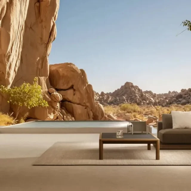 Modern living room with a gray sectional, wooden coffee table, and a desert landscape view through a large window; a wall-mounted image of an astronaut is on the left.