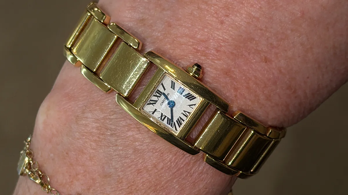 Gold bracelet watch with a rectangular Roman numeral dial on a person’s wrist (close-up).