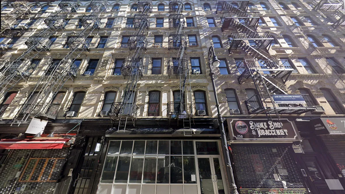 Multi-story brick building with numerous exterior metal fire escapes on a bustling urban street. storefronts line the ground floor, including a smoke shop sign.
