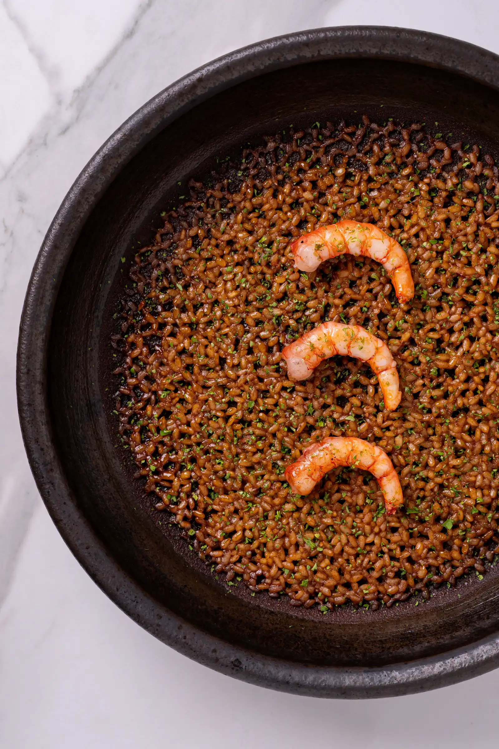 Brown lentils in a dark skillet, topped with three shrimp as garnish
