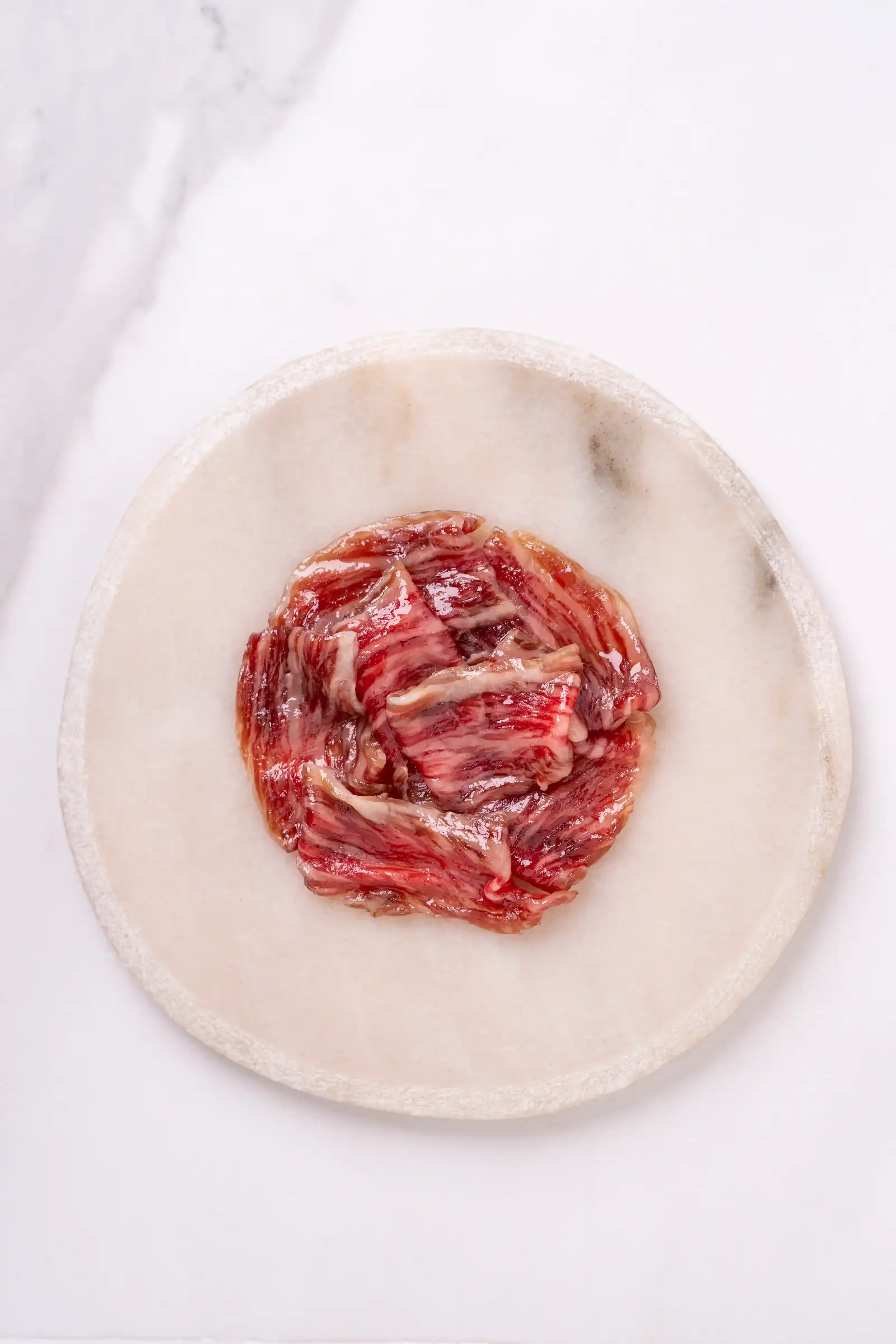 Pile of thinly sliced raw beef arranged in a circle on a white marble plate.
