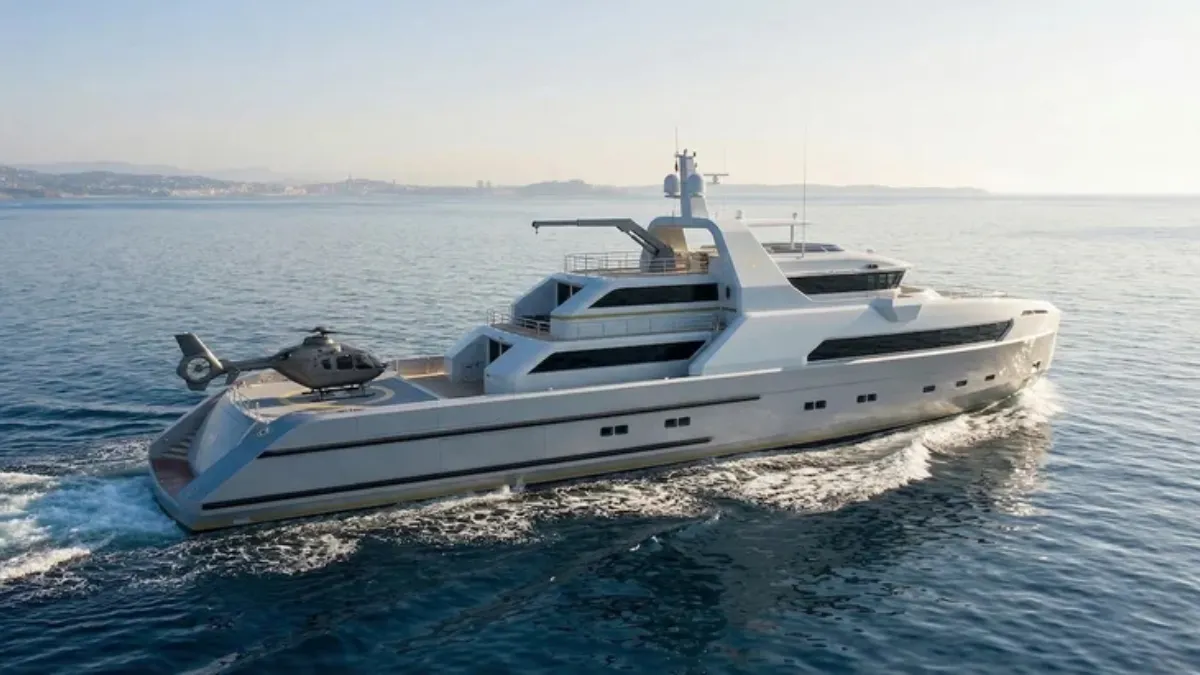 White luxury motor yacht sailing on calm blue sea with a helicopter on its aft deck.