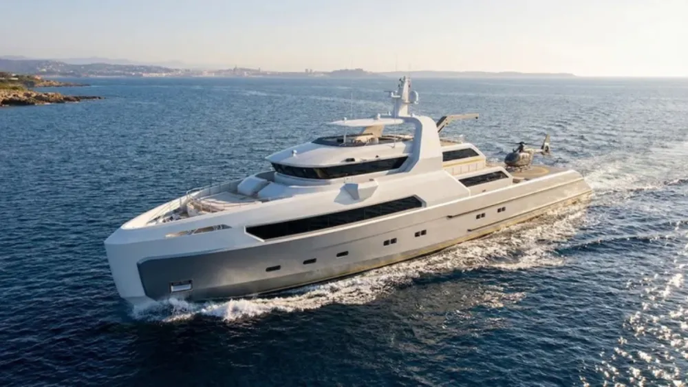 White luxury motor yacht sailing in calm blue water near a rocky coastline at sunset/sunlit horizon