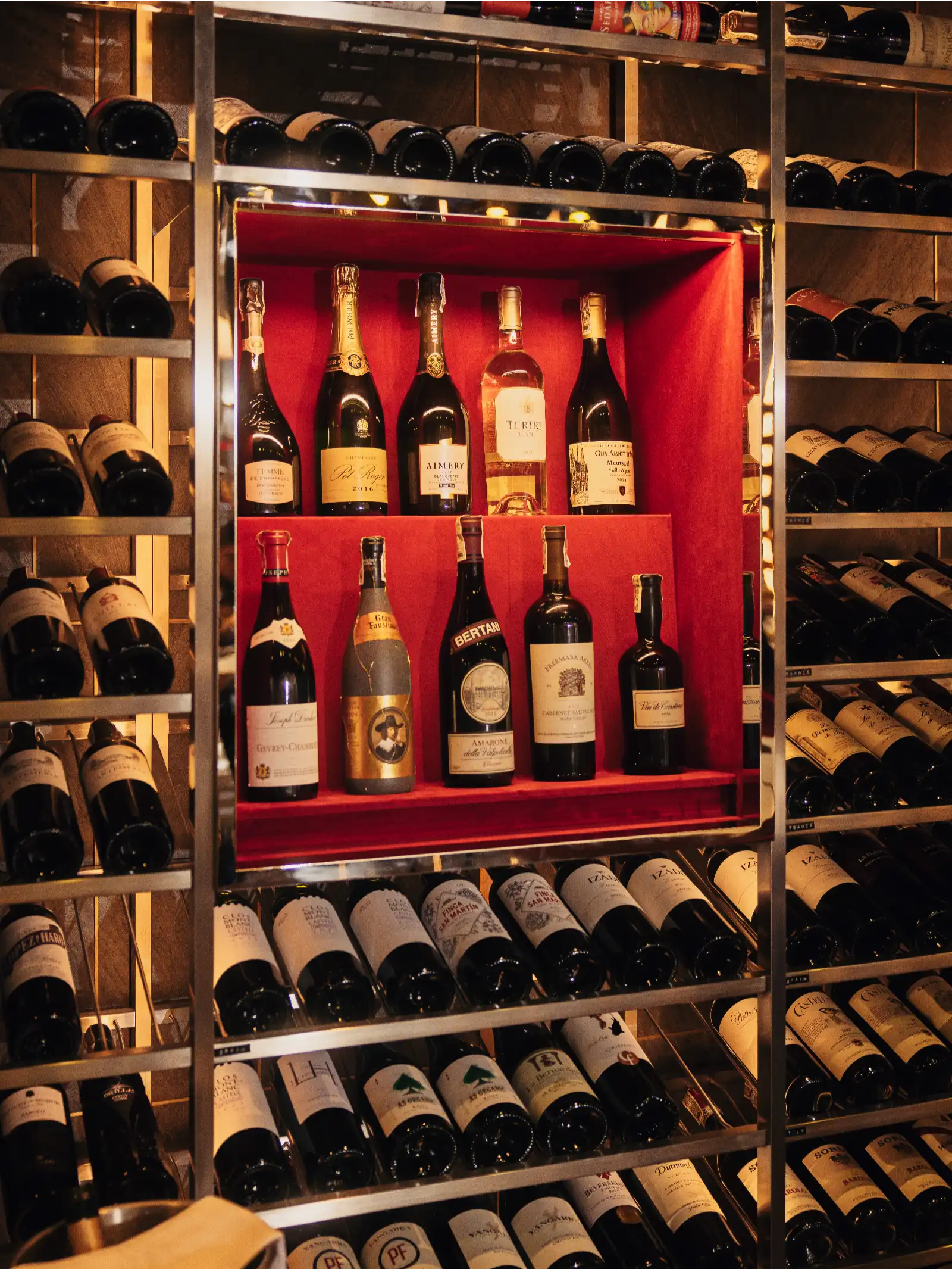 Rows of wine bottles on metal racks in a wine cellar, with a red central display case.