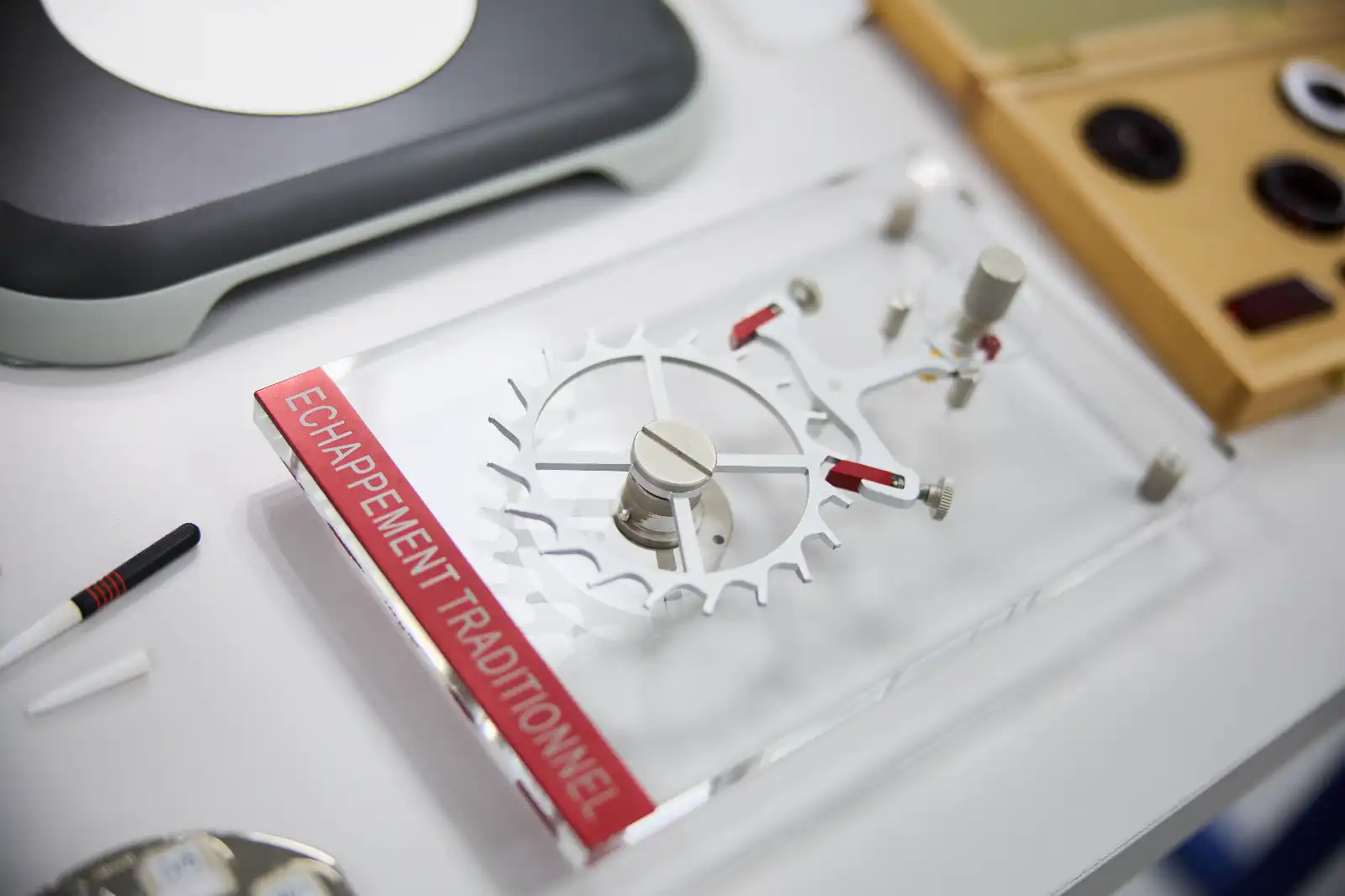 Close-up of a white gear with teeth and red adjustment levers on a white lab bench.