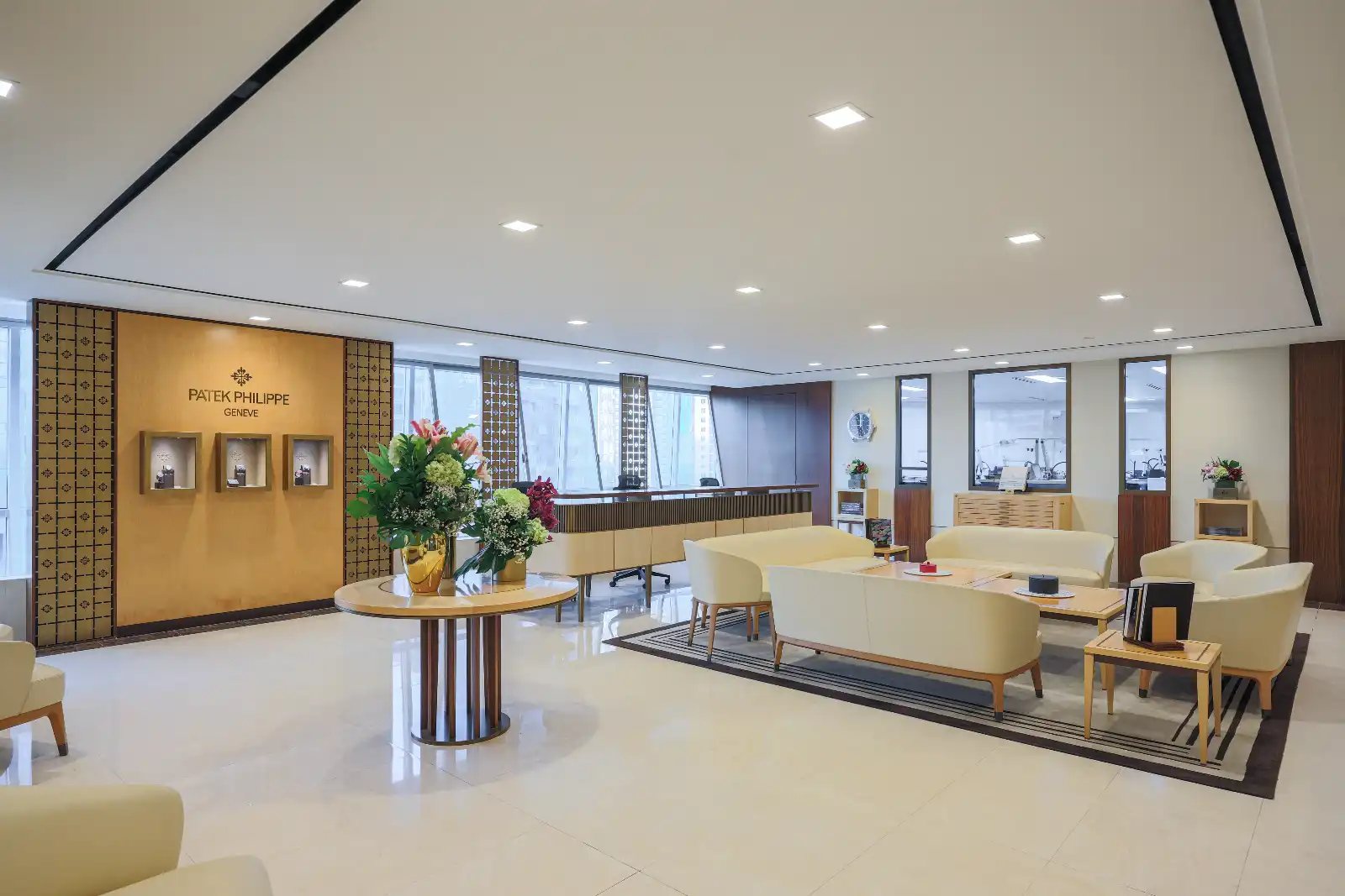 Luxurious showroom lobby with cream seating, a round flower table, and a Patek Philippe display wall.
