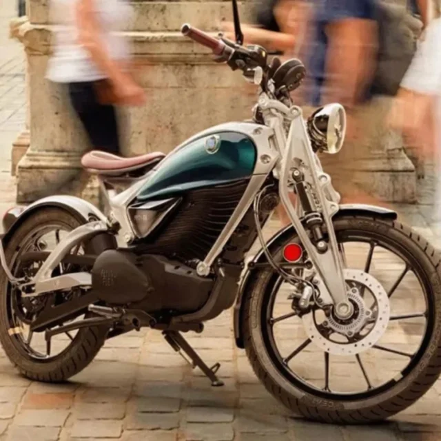 Teal and black cruiser motorcycle parked on a cobblestone square as blurred pedestrians pass by.
