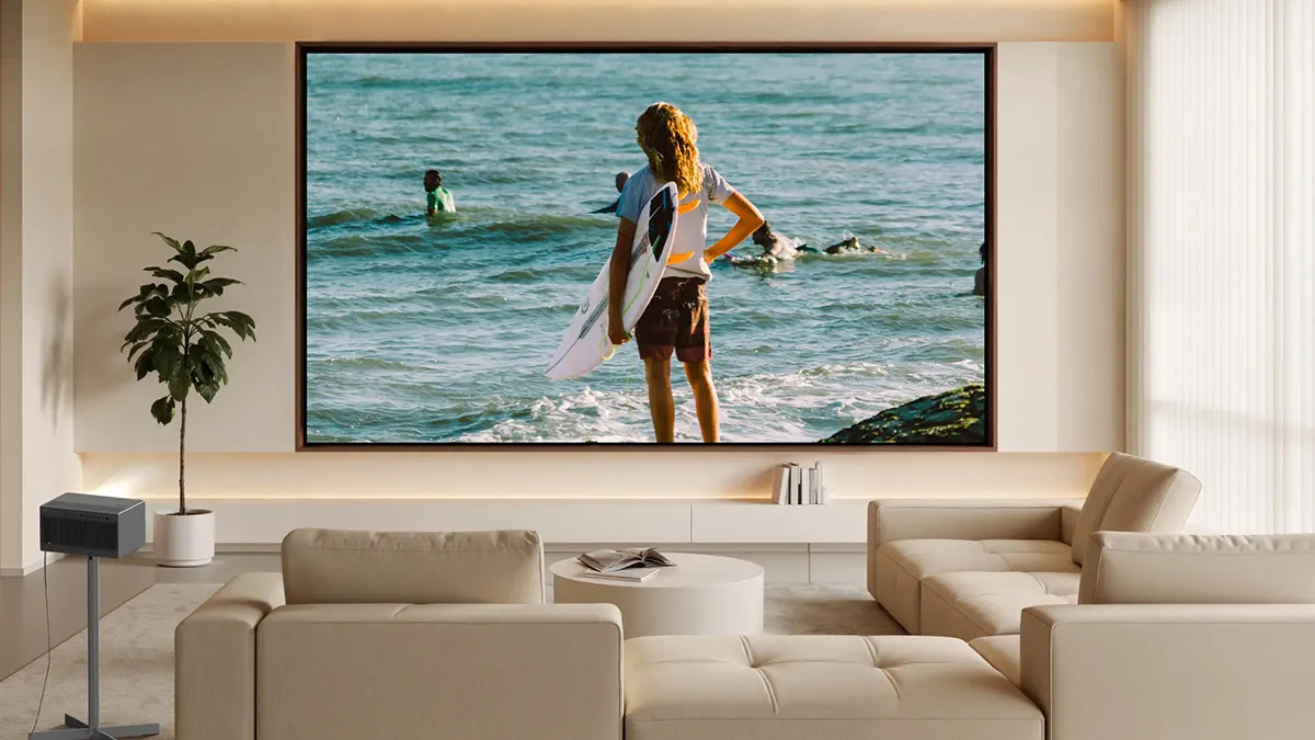 Living room with a large wall-mounted screen showing a surfer holding a board at the beach, beige seating, and a minimalist neutral design.