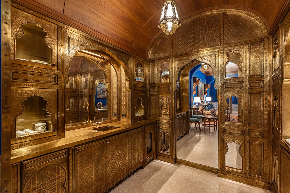 Gold-embossed ornate kitchen cabinetry with arches and a sink, opening to a blue living room beyond.