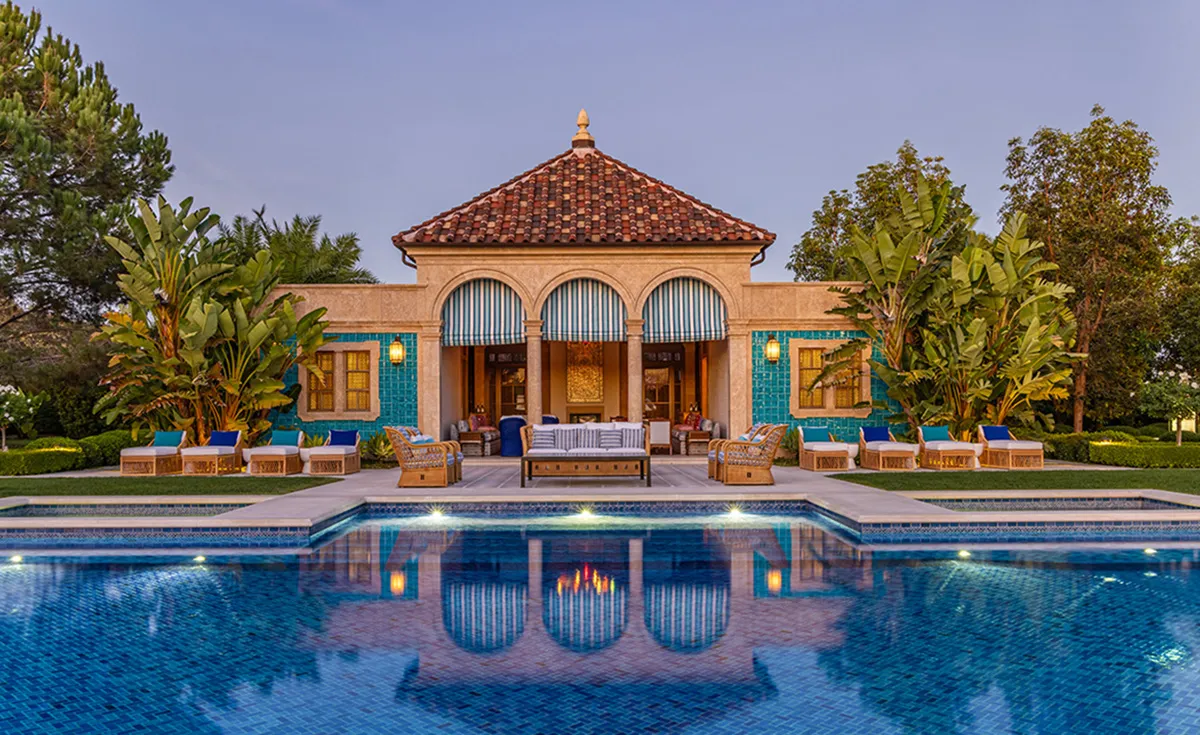 Luxurious villa with a terracotta-tiled roof, teal walls, and a large outdoor pool reflecting the building.