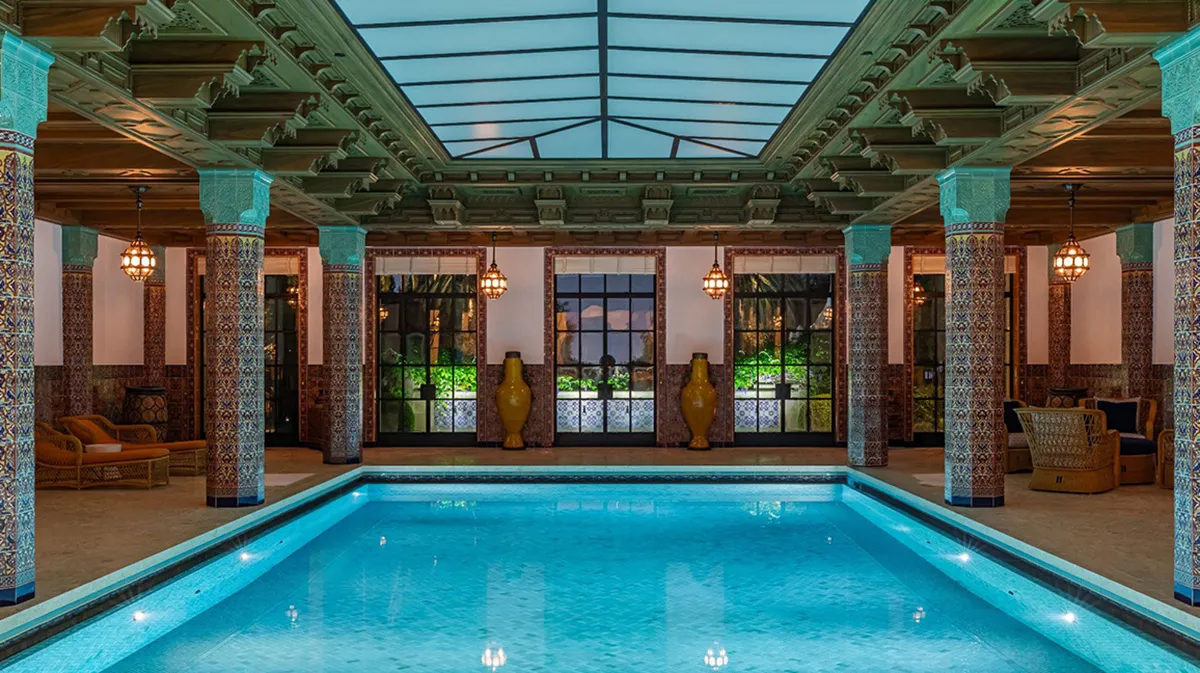 Indoor luxurious pool area with turquoise mosaic columns, glass skylight, and teal-lit pool.