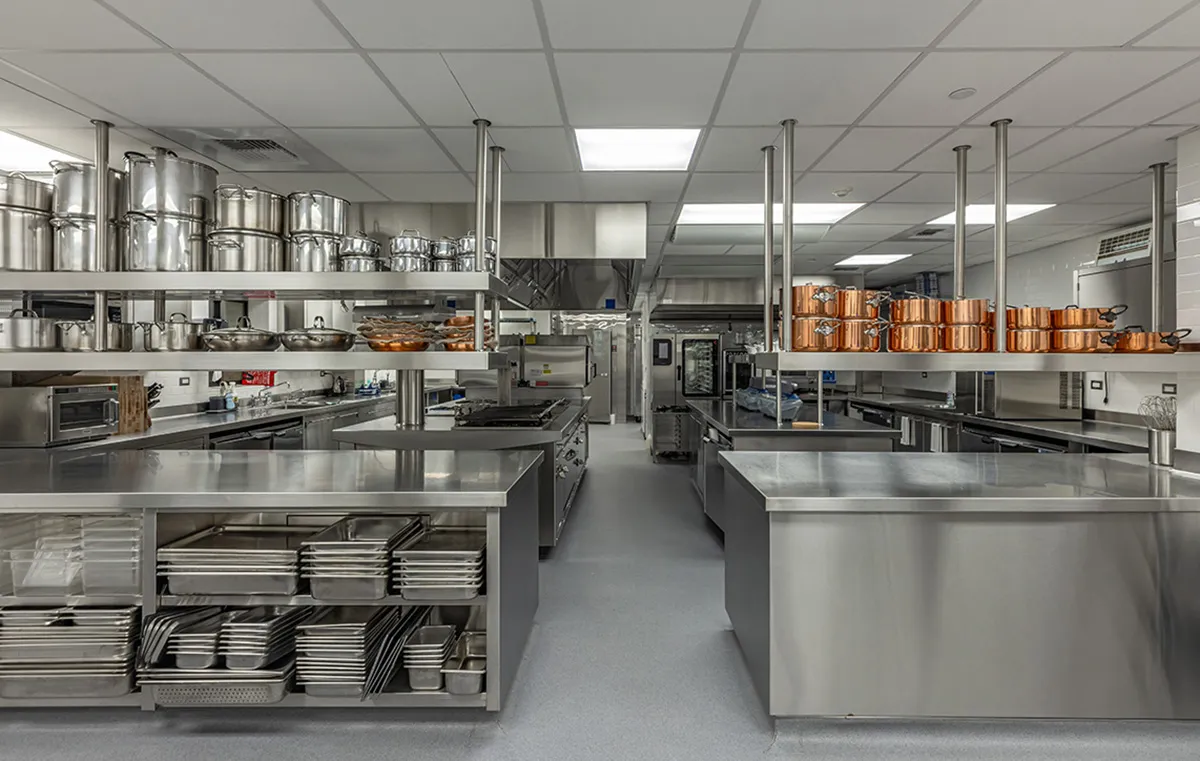 Professional commercial kitchen with stainless steel worktables, shelving, and copper pots lined along a central prep area