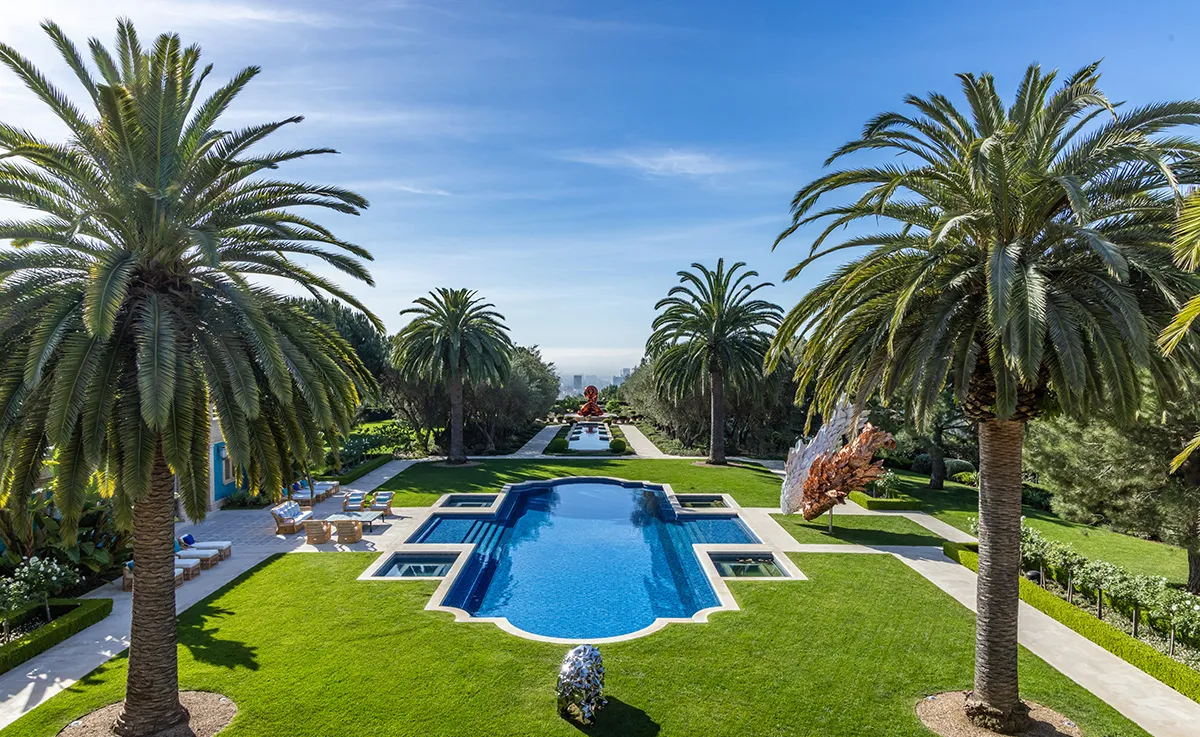 Luxurious rectangular pool framed by palm trees and a neatly trimmed lawn on a sunny day.