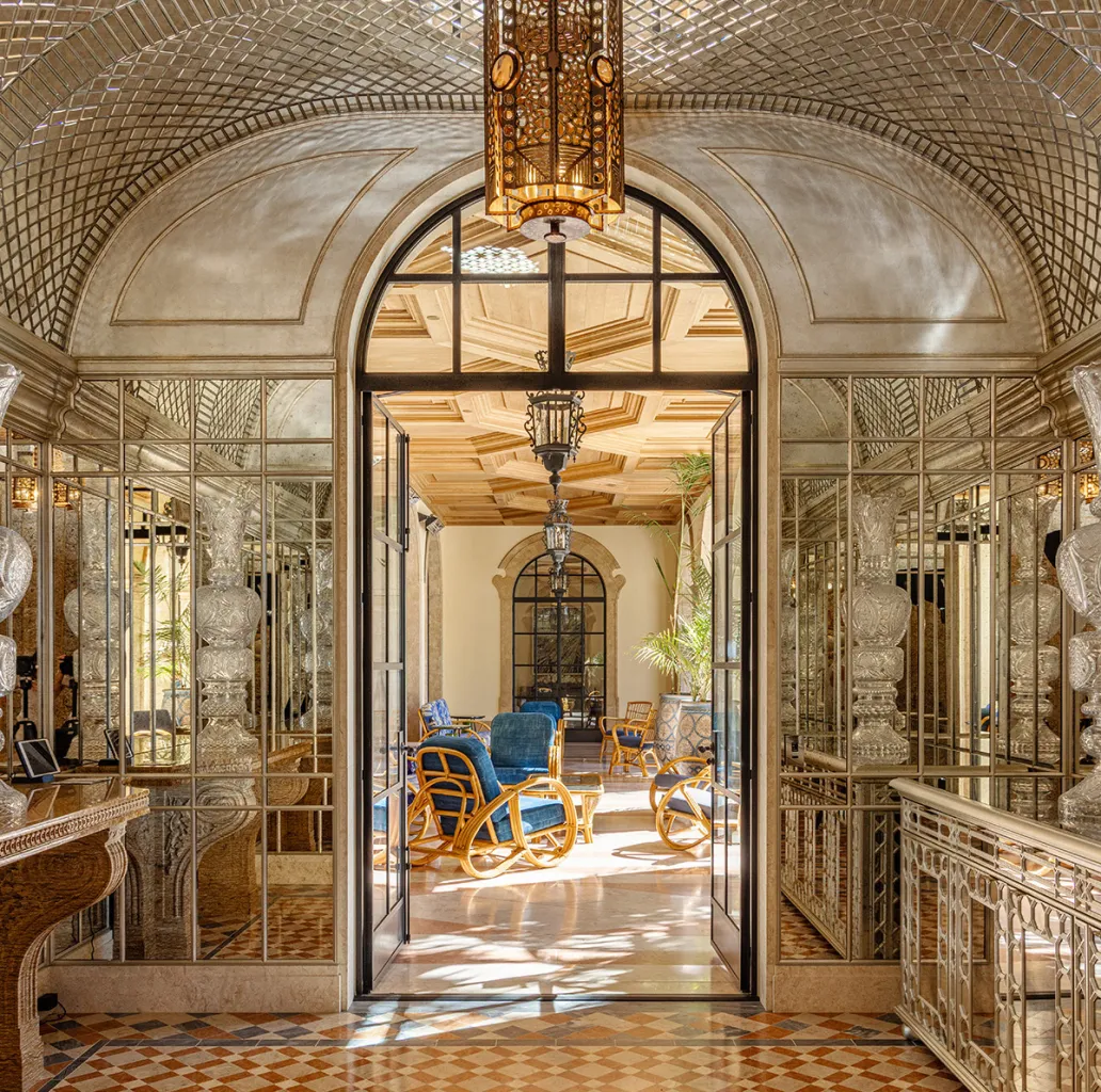 Ornate mirrored hallway opening into a sunlit lounge with blue cushioned wicker chairs