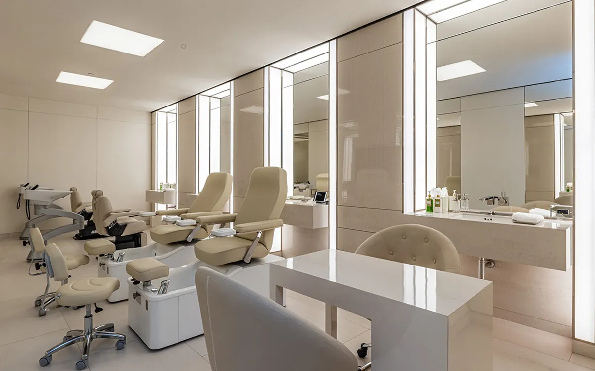 Modern beauty clinic treatment room with beige reclining chairs and mirrored vanity stations along a bright wall.