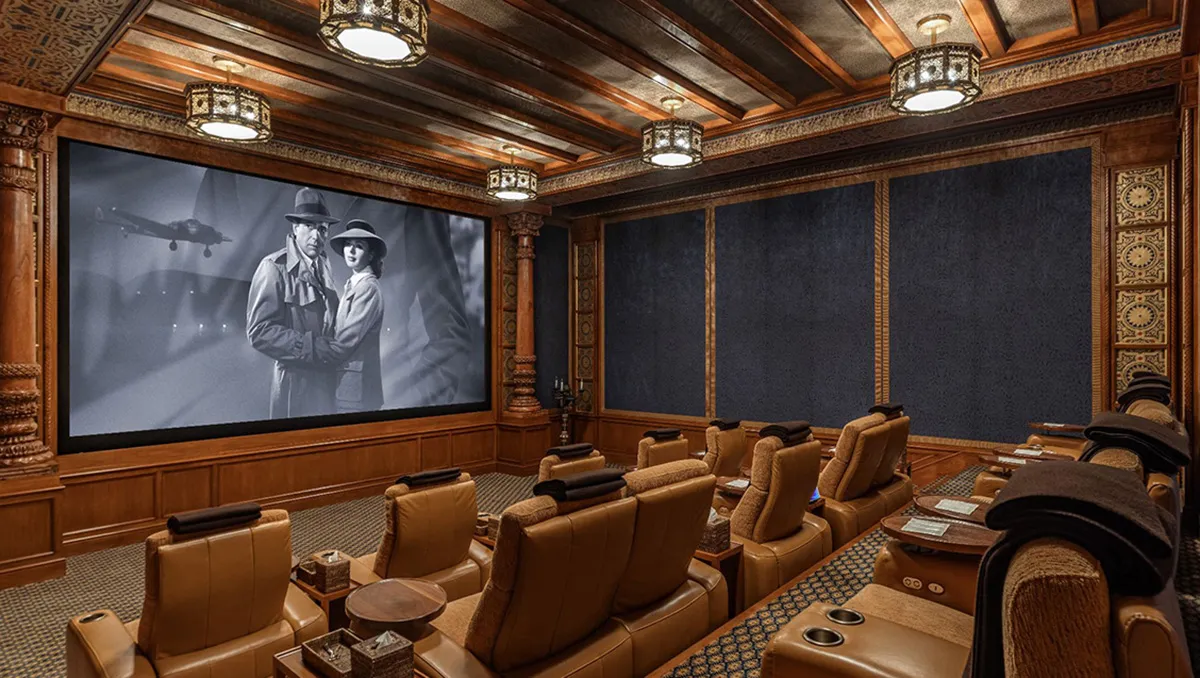 Luxurious home theater with brown leather recliners, wood paneling, and a large screen showing a black-and-white film.