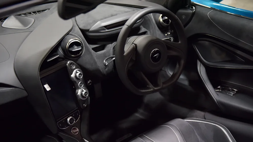 Close-up of a luxurious black car interior, highlighting the steering wheel, center console, and stitched leather seats and panels.