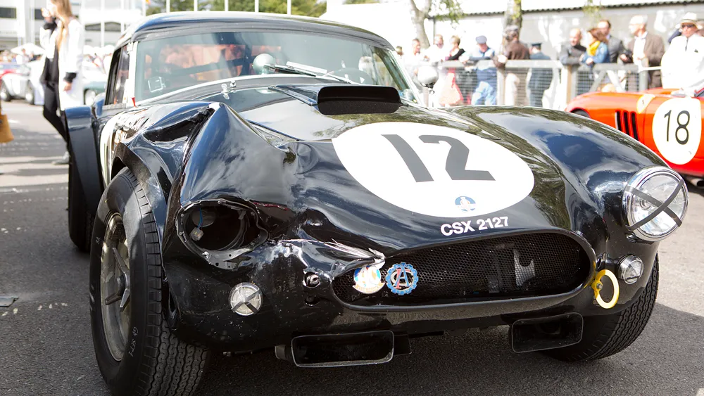 Black vintage race car with the number 12 on the hood and front-end damage at a car show. сут