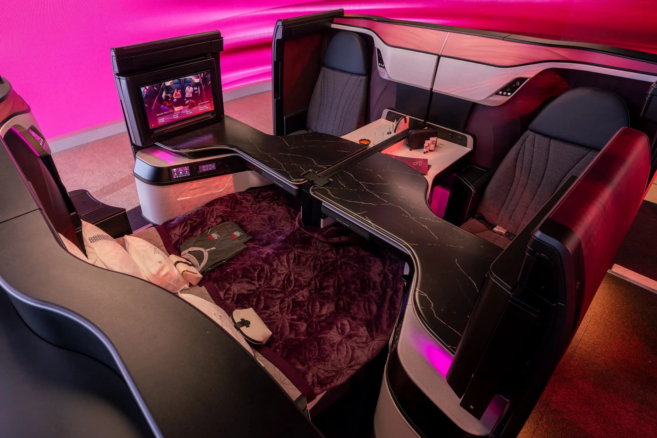 Luxurious business-class airplane cabin with a long marble-finish bed and pink mood lighting.
