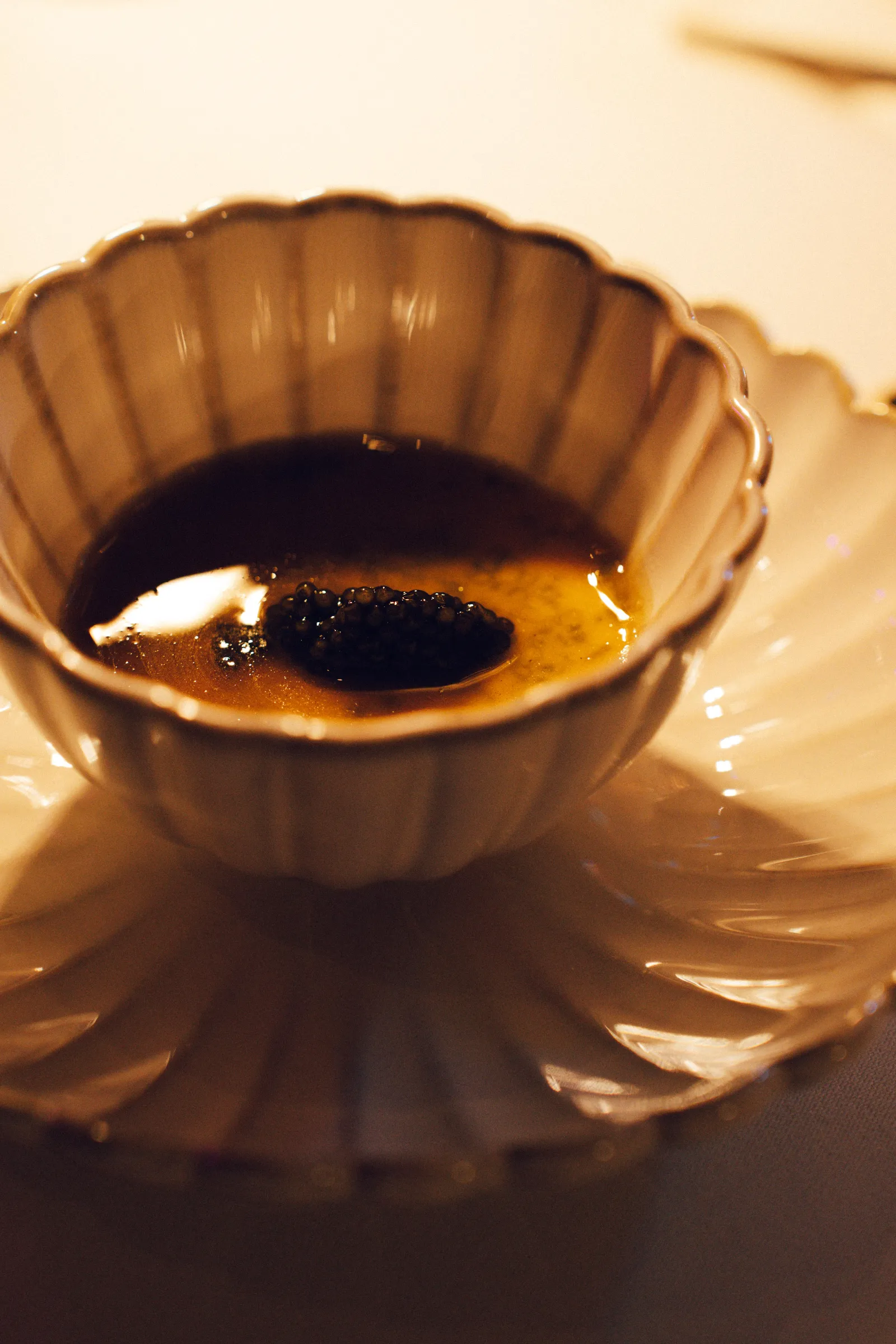 Close-up of a white scalloped teacup filled with dark coffee on a matching saucer.